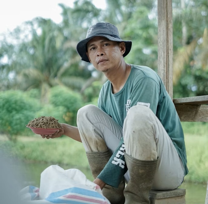 man sat down holding a bowl filled with soil