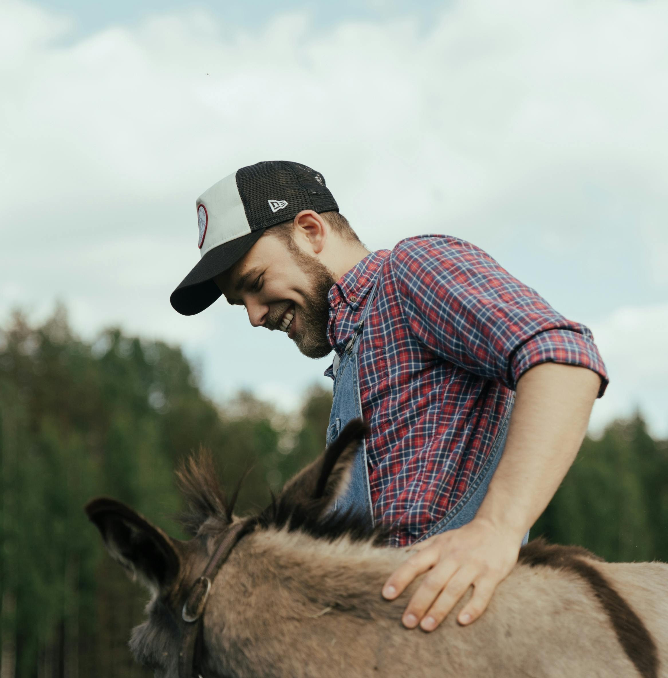 a man with a hat smiling at his donkey